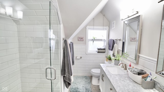 bathroom with a shower stall, a wainscoted wall, toilet, vanity, and tile walls