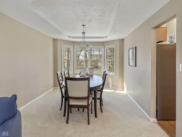 dining room featuring a textured ceiling, light carpet, and a tray ceiling