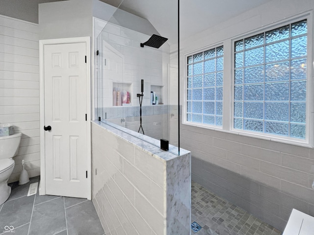 bathroom featuring a tile shower, tile patterned flooring, and toilet