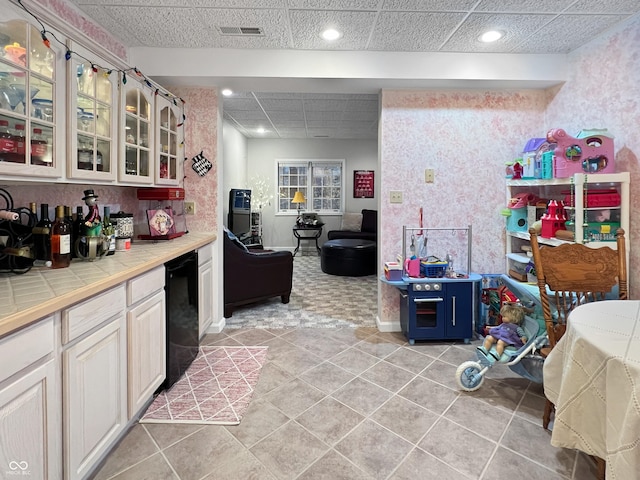 kitchen featuring a paneled ceiling, tile countertops, dishwasher, light tile patterned floors, and white cabinetry