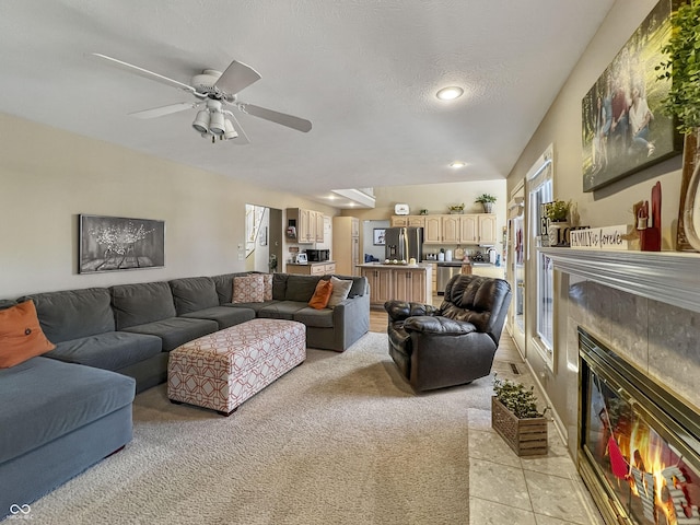 living room featuring a textured ceiling, a tiled fireplace, light carpet, and ceiling fan