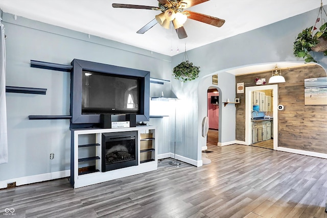 unfurnished living room featuring a fireplace, hardwood / wood-style flooring, ceiling fan, and wooden walls