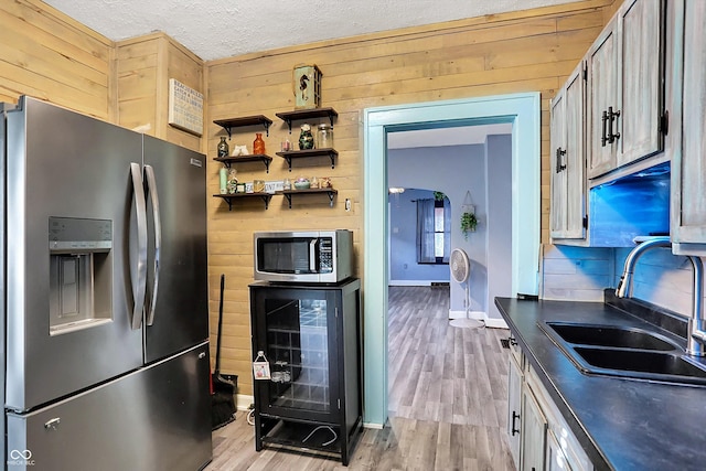 kitchen with light hardwood / wood-style floors, sink, stainless steel appliances, and wooden walls