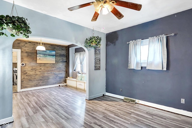 unfurnished room featuring ceiling fan, wood walls, wood-type flooring, and a wealth of natural light