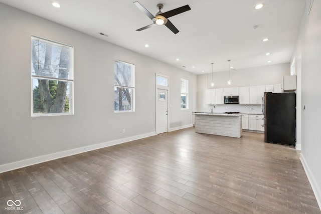 kitchen featuring black refrigerator, white cabinetry, a healthy amount of sunlight, and an island with sink