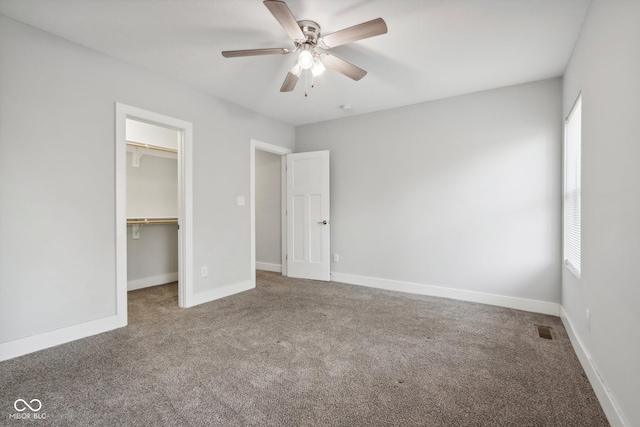 unfurnished bedroom featuring carpet, a walk in closet, a closet, and ceiling fan