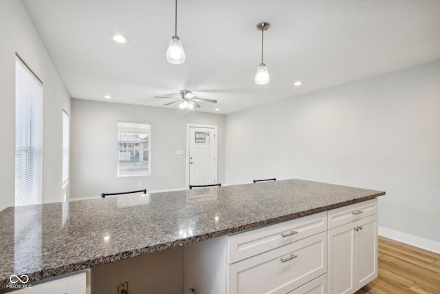 kitchen featuring white cabinets, decorative light fixtures, light hardwood / wood-style floors, and dark stone countertops