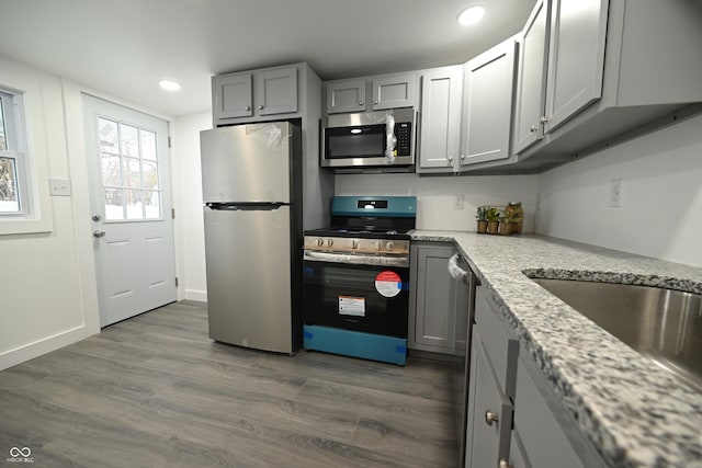 kitchen with gray cabinets, light stone counters, dark wood-type flooring, and stainless steel appliances