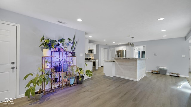 kitchen with appliances with stainless steel finishes, pendant lighting, white cabinets, light hardwood / wood-style floors, and a kitchen island