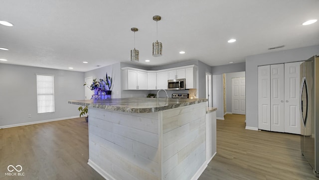 kitchen with white cabinets, stainless steel appliances, decorative light fixtures, and light hardwood / wood-style floors