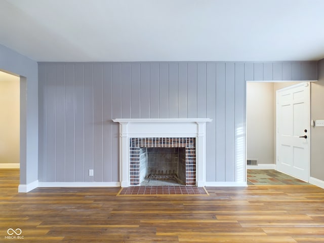 unfurnished living room featuring a tiled fireplace, wood walls, and wood-type flooring