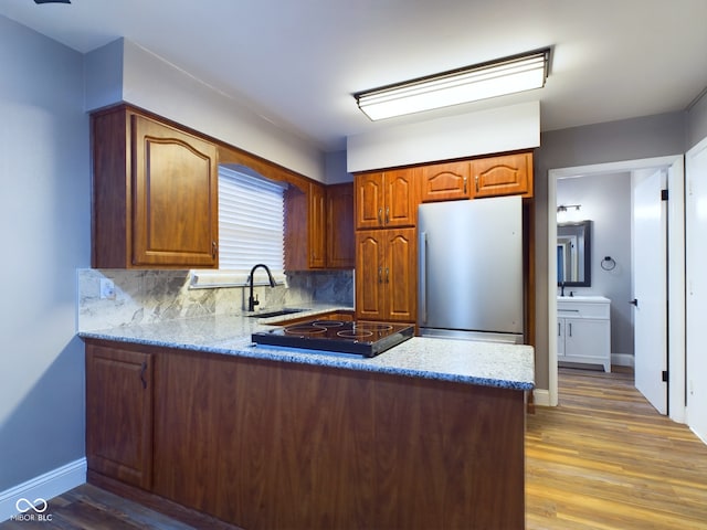 kitchen with stainless steel refrigerator, sink, tasteful backsplash, light hardwood / wood-style flooring, and kitchen peninsula