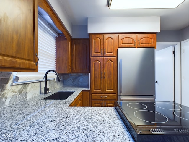 kitchen featuring sink, tasteful backsplash, light stone counters, stainless steel fridge, and stovetop