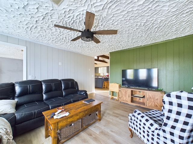 living room with a textured ceiling, hardwood / wood-style flooring, ceiling fan, and wooden walls