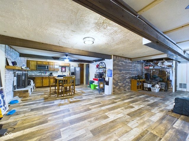 interior space with wood-type flooring, stainless steel fridge with ice dispenser, a textured ceiling, and brick wall