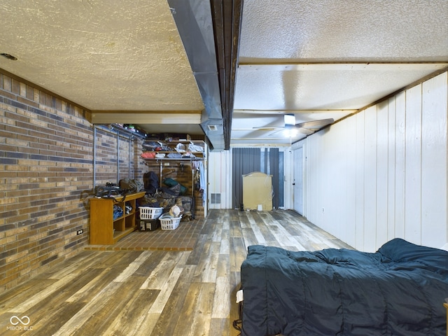 basement featuring hardwood / wood-style flooring, brick wall, a textured ceiling, and wooden walls