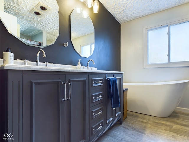 bathroom with a bathing tub, wood-type flooring, vanity, and a healthy amount of sunlight