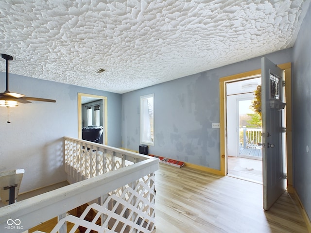 corridor featuring plenty of natural light, wood-type flooring, and a textured ceiling