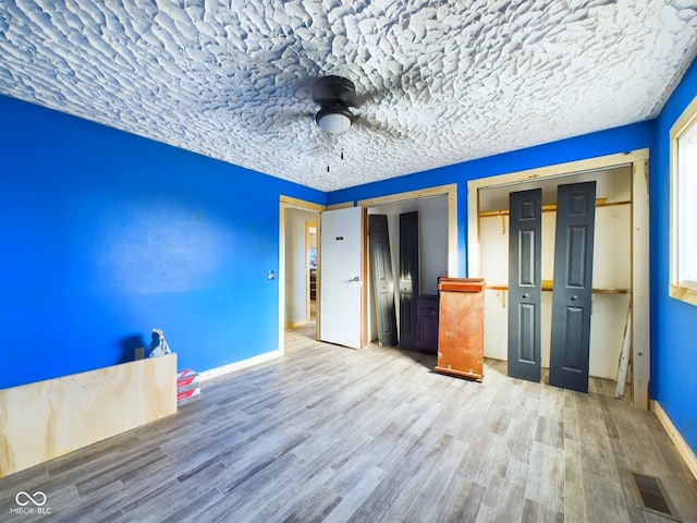 unfurnished bedroom with a textured ceiling, ceiling fan, hardwood / wood-style floors, and two closets