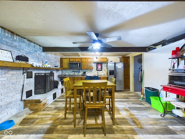 dining space featuring brick wall, a textured ceiling, ceiling fan, hardwood / wood-style flooring, and a fireplace