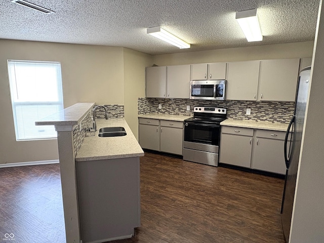 kitchen with dark hardwood / wood-style floors, kitchen peninsula, sink, and appliances with stainless steel finishes