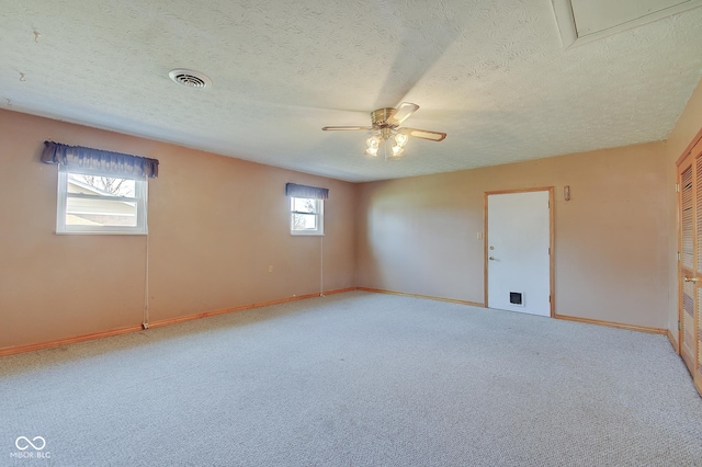 carpeted spare room featuring a textured ceiling, a wealth of natural light, and ceiling fan