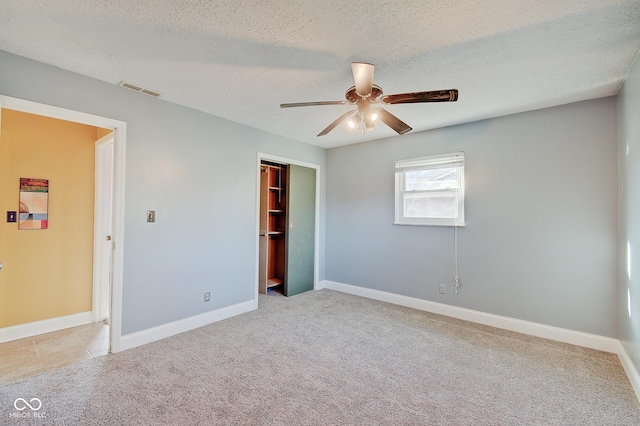 unfurnished bedroom with ceiling fan, a closet, light colored carpet, and a textured ceiling