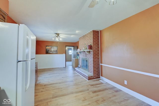 kitchen featuring a brick fireplace, ceiling fan, white fridge, and light hardwood / wood-style flooring