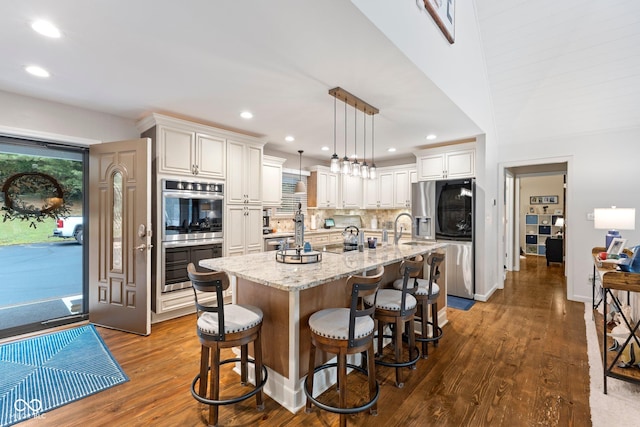 kitchen with pendant lighting, dark hardwood / wood-style floors, a kitchen island with sink, and appliances with stainless steel finishes