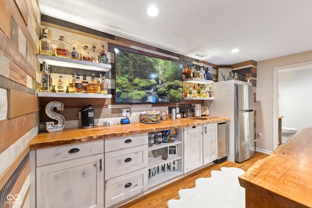 bar featuring stainless steel fridge, sink, light hardwood / wood-style flooring, white cabinets, and butcher block counters