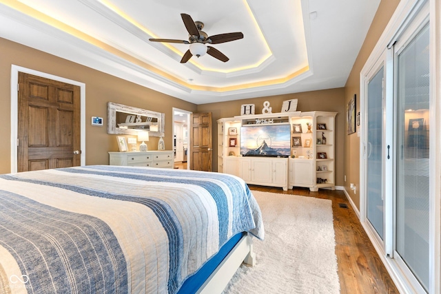 bedroom featuring ceiling fan, wood-type flooring, and a tray ceiling