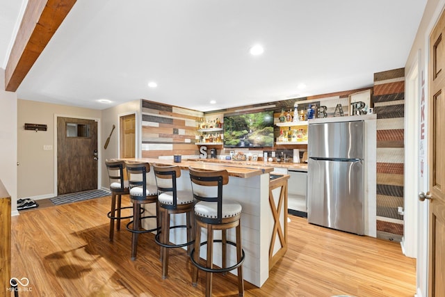 kitchen featuring a kitchen bar, appliances with stainless steel finishes, light wood-type flooring, and wooden counters