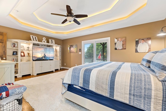 bedroom with ceiling fan, access to exterior, light hardwood / wood-style flooring, and a tray ceiling