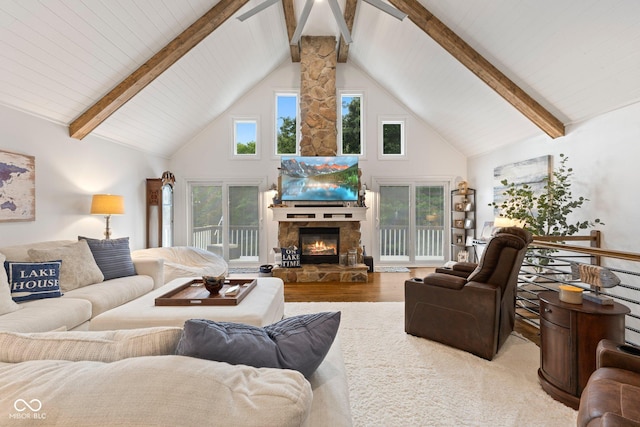 living room featuring beam ceiling, light wood-type flooring, high vaulted ceiling, and a stone fireplace