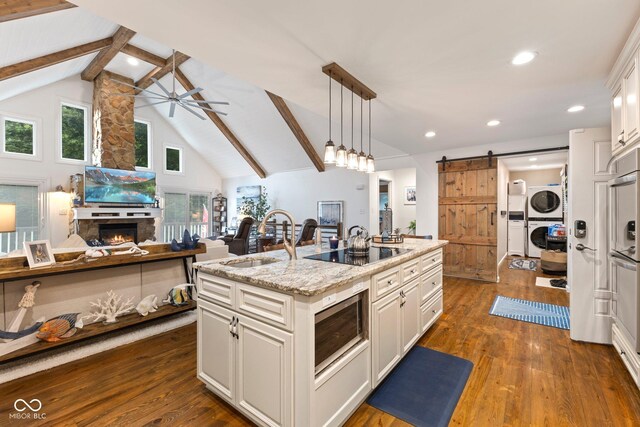 kitchen with black electric stovetop, a kitchen island with sink, a barn door, stacked washer and dryer, and hanging light fixtures