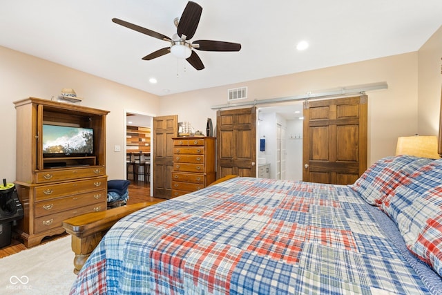 bedroom with ceiling fan, a barn door, and wood-type flooring