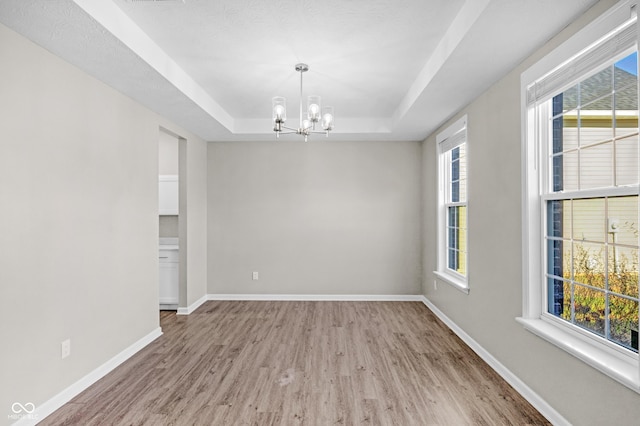 spare room with hardwood / wood-style floors, an inviting chandelier, and a raised ceiling