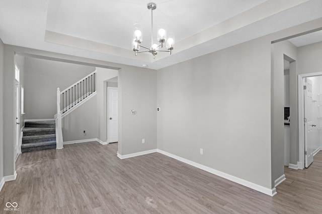 unfurnished living room featuring wood-type flooring, an inviting chandelier, and a raised ceiling