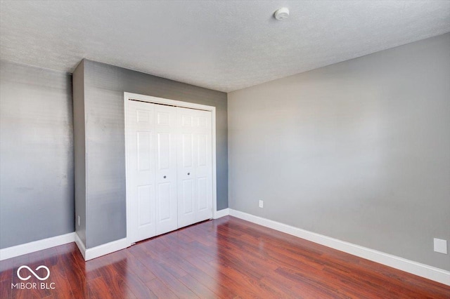 unfurnished bedroom featuring a textured ceiling, dark wood-type flooring, and a closet