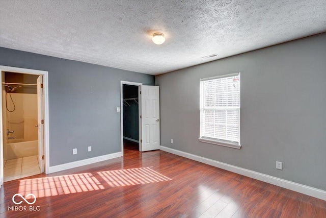 unfurnished bedroom with connected bathroom, wood-type flooring, a textured ceiling, a walk in closet, and a closet