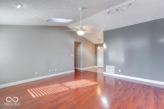 empty room with lofted ceiling with skylight, ceiling fan, wood-type flooring, and a textured ceiling