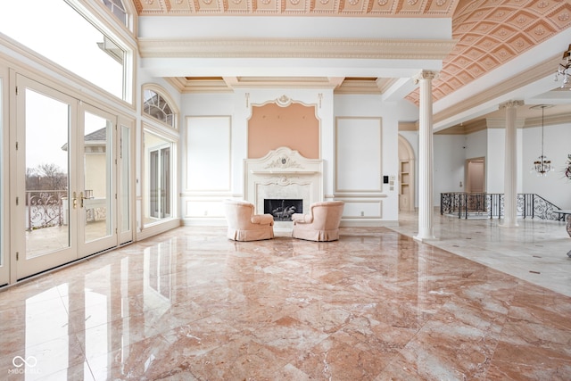 unfurnished living room featuring french doors, a towering ceiling, ornate columns, ornamental molding, and a fireplace