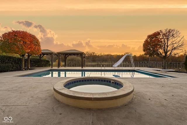 pool at dusk featuring a gazebo, an in ground hot tub, a water slide, and a diving board