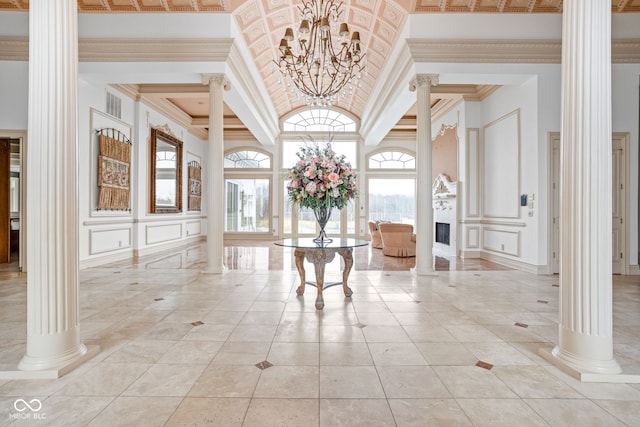 tiled foyer entrance featuring ornate columns, a towering ceiling, ornamental molding, and an inviting chandelier