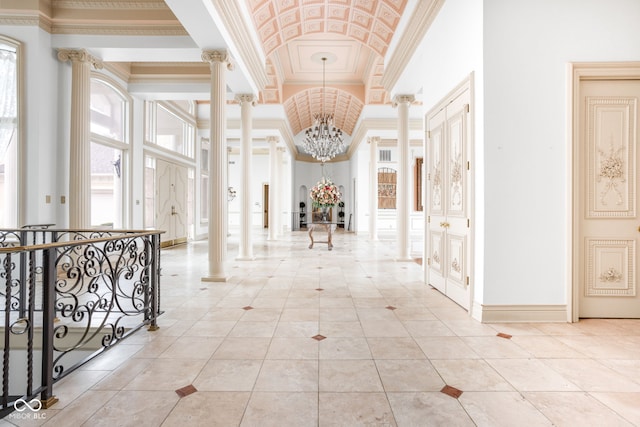 hallway featuring an inviting chandelier, light tile patterned floors, ornate columns, ornamental molding, and a towering ceiling