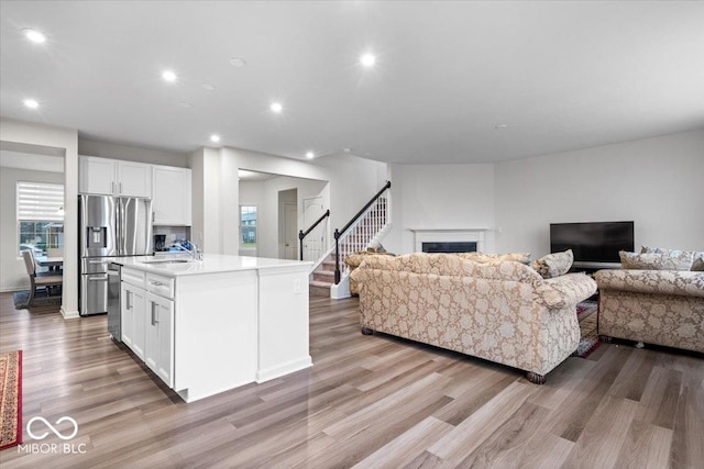 kitchen with sink, an island with sink, appliances with stainless steel finishes, light hardwood / wood-style floors, and white cabinetry