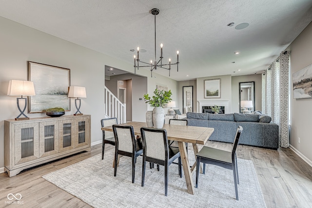 dining room with a notable chandelier, a fireplace, light wood finished floors, a textured ceiling, and stairs