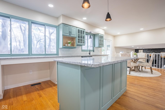 kitchen with backsplash, light stone counters, pendant lighting, light hardwood / wood-style flooring, and a kitchen island