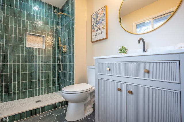 bathroom featuring tile patterned flooring, a tile shower, vanity, and toilet