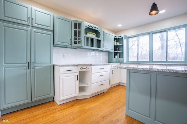 kitchen featuring light stone countertops, tasteful backsplash, decorative light fixtures, white cabinets, and light wood-type flooring